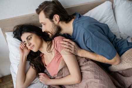 High angle view of bearded man looking at indifferent girlfriend on bed in morning 
