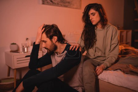 Caring brunette woman calming down sad boyfriend in bedroom in evening 