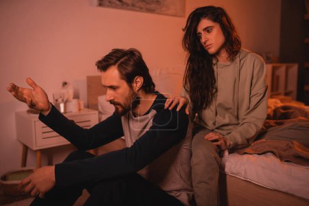Brunette woman calming down upset boyfriend talking in bedroom in evening 