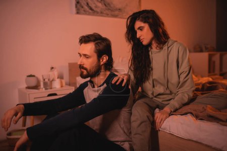 Caring woman touching shoulder of upset boyfriend in bedroom at home 