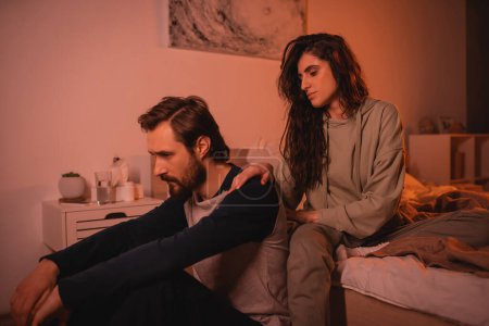 Upset man receiving care from caring girlfriend in bedroom in evening 