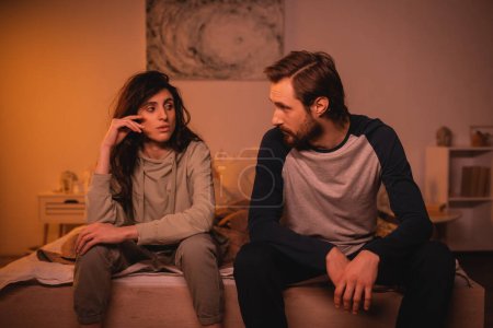 Dissatisfied woman talking to bearded boyfriend on bed in evening 