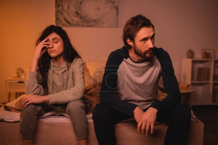 Sad couple with relationship difficulties sitting on bed in evening 