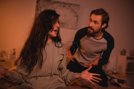 Foto de Hombre enojado discutiendo con novia nerviosa en el dormitorio por la noche - Imagen libre de derechos