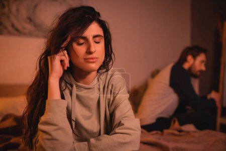 Displeased woman sitting near blurred boyfriend on bed at home 