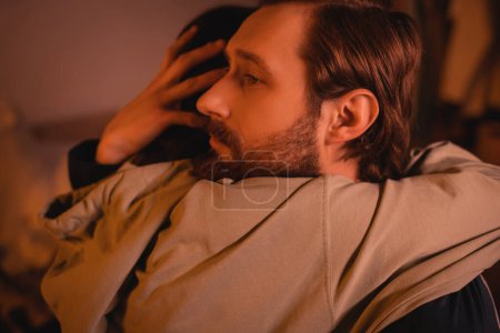 Caring man hugging girlfriend at home with red lighting in evening 