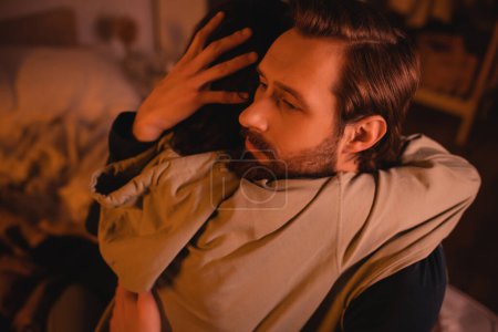 Bearded man hugging girlfriend at home with red lighting  
