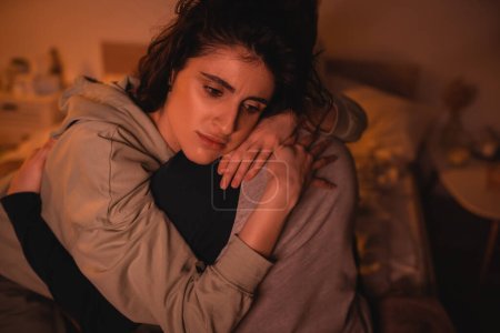 Sad woman hugging boyfriend in bedroom at night 