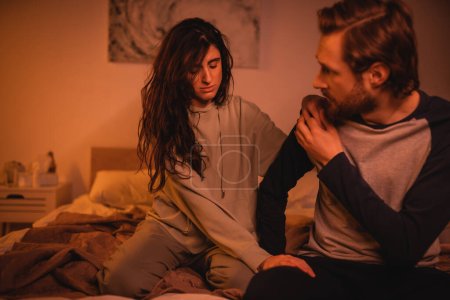 Brunette woman calming down boyfriend on bed in evening 