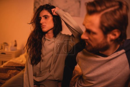 Téléchargez les photos : Femme pensive assise près du petit ami flou pendant les difficultés relationnelles à la maison - en image libre de droit