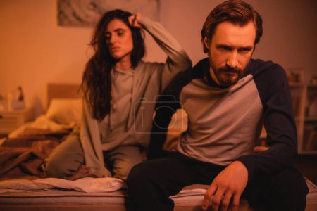Displeased man sitting near blurred girlfriend during relationship difficulties at home 