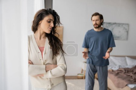 Empörte Frau verschränkt die Arme, während sich ihr unscharfer Freund zu Hause streitet 