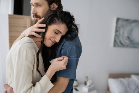 Empathic man calming crying girlfriend in blurred bedroom at home 
