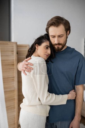 Sad couple in pajama hugging at home in morning 