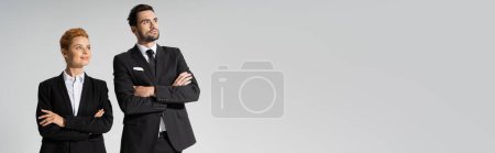 Photo for Happy redhead businesswoman and confident businessman looking away isolated on grey, banner - Royalty Free Image