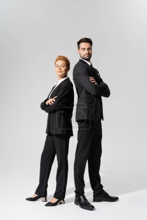 full length of incredulous business people standing back to back with folded arms on grey background