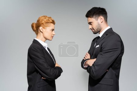 Photo for Side view of angry business people looking at each other while standing with crossed arms isolated on grey - Royalty Free Image