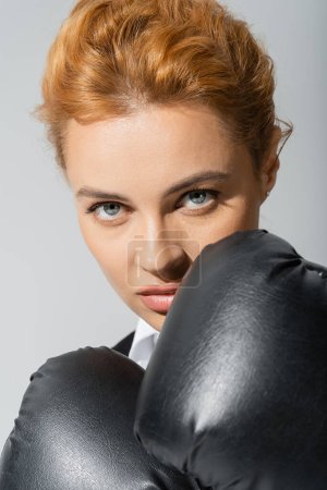Porträt einer selbstbewussten Geschäftsfrau in Boxhandschuhen, die isoliert auf grau in die Kamera blickt