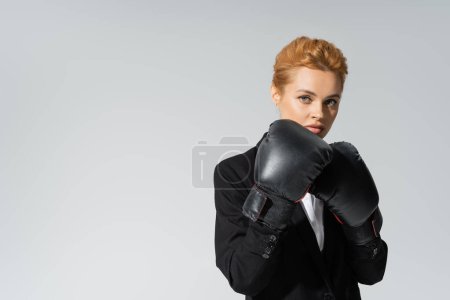 empresaria intencional en guantes de boxeo mirando a la cámara aislada en gris