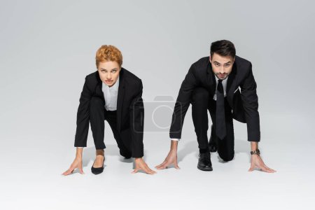 gente de negocios con estilo en trajes negros de pie en posición de inicio bajo y mirando a la cámara en el fondo gris