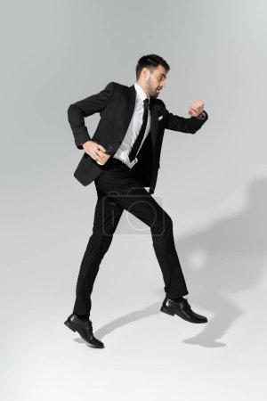 Foto de Longitud completa de hombre de negocios en traje elegante comprobar el tiempo y levitar sobre fondo gris - Imagen libre de derechos
