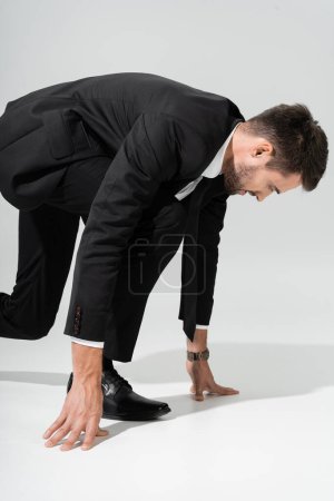 Foto de Vista lateral del empresario con propósito en traje negro de pie en posición de inicio bajo sobre fondo gris - Imagen libre de derechos