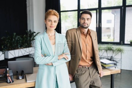 positive business colleagues standing at work desk in modern office and looking at camera