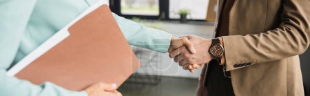partial view of woman with folder shaking hands with businessman in office, banner