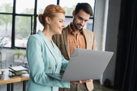 socios de negocios sonrientes en ropa de moda mirando a la computadora portátil en la oficina