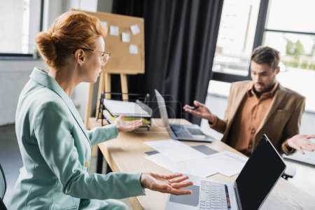 confused manager showing shrug gesture near documents and businesswoman in office
