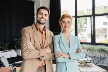 Photo for Successful business colleagues in stylish suits standing with folded arms and smiling at camera in office - Royalty Free Image