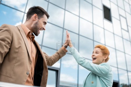 Photo for Overjoyed business partners giving high five near modern building on urban street - Royalty Free Image