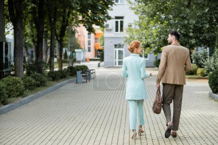 Rückansicht stilvoller Geschäftskollegen, die sich beim Spaziergang durch die grüne Gasse in der Stadt unterhalten