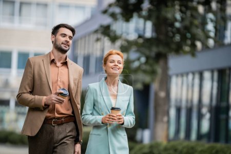 Photo for Cheerful and stylish business colleagues with coffee to go smiling and looking away on blurred urban street - Royalty Free Image