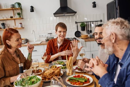 happy gay man showing wedding ring to parents during family supper in kitchen