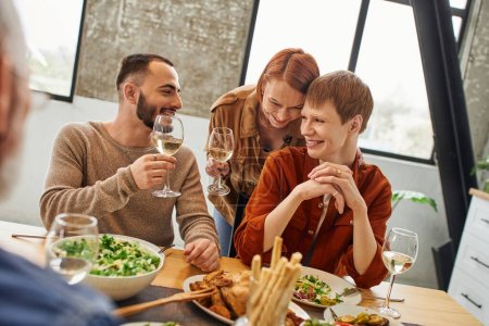 happy redhead woman toasting with wine near son and bearded gay man during family supper at home 