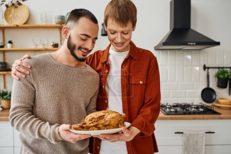 happy gay man embracing boyfriend while holding grilled chicken in kitchen