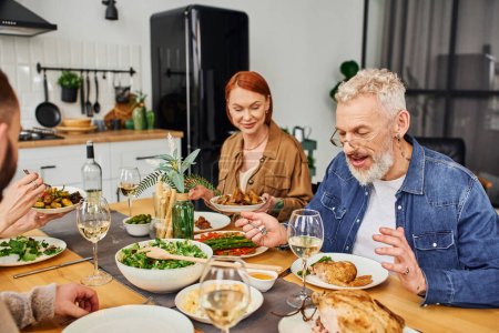 cheerful bearded man in eyeglasses talking to family while having delicious dinner in kitchen