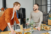 happy gay couple looking at each other near prepared supper in modern kitchen t-shirt #653456394