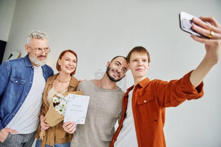 happy gay man taking selfie with boyfriend and parents holding flowers and wedding invitation card