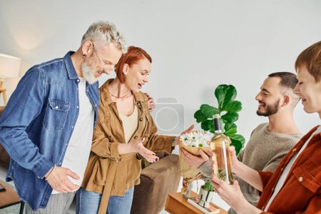 junges schwules Paar besucht glückliche Eltern zu Hause, während es Blumen und eine Flasche Wein in der Hand hält