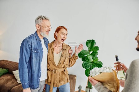 amazed woman showing wow gesture near gay couple with flowers and wine bottle at home