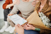 selective focus of wedding invitation near young gay couple and parents sitting at home tote bag #653456874