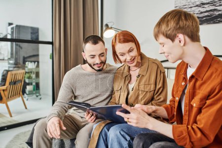 Photo for Redhead gay man showing photo album to boyfriend and amazed mother at home - Royalty Free Image