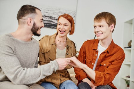 aufgeregte Frau lacht neben schwulem Mann und Sohn und zeigt Ehering zu Hause