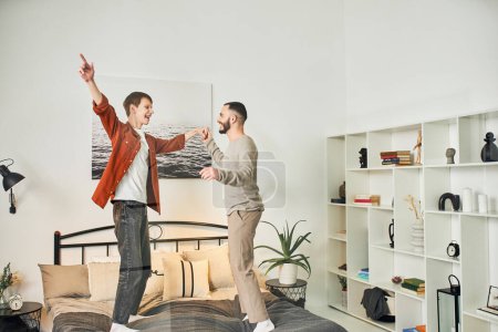 overjoyed gay couple having fun while standing on bed at home