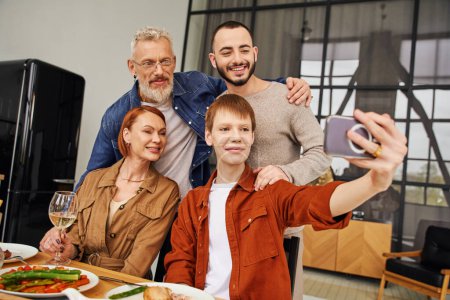 rothaariger schwuler Mann macht Selfie mit glücklichen Eltern und Freund beim Familienessen zu Hause