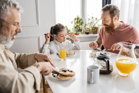 preteen girl having breakfast with gay parents at home in morning 