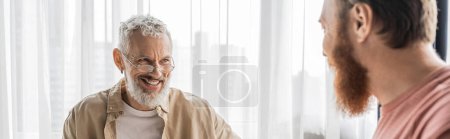 Senior gay man smiling at blurred partner at home, banner 