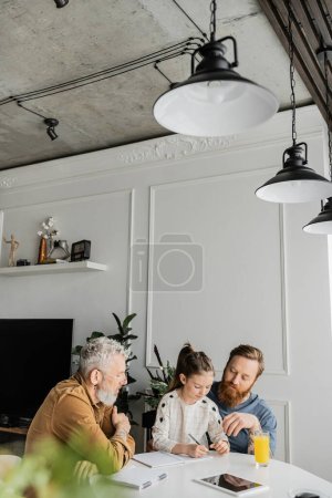 Padres homosexuales ayudando a su hija con la tarea cerca de la tableta digital y el jugo de naranja en casa 